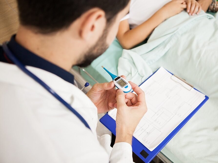 A doctor checking a patient’s temperature with a digital thermometer during a clinical examination, representing quality care by the Best General Physician in Indore.